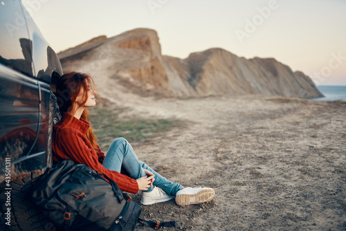woman hiker in the mountains on nature sits near the car and mountains in the background sky road landscape
