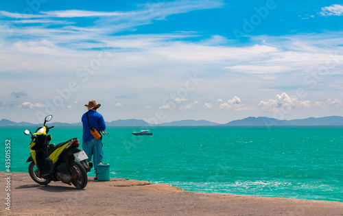 Koh Larn island. A man is fishing in the sea at Koh Lan amid the clear sky and emerald green water.