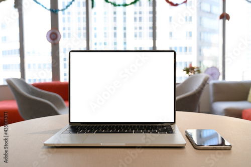 front view of laptop with blank screen on the wooden table with mobile phone. Laptop for working in the office environment.