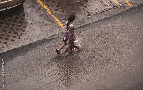 An Indian girl walks through the streets flooded with rain water on rainy day in the city. Girl splashing water in a puddle on the road.