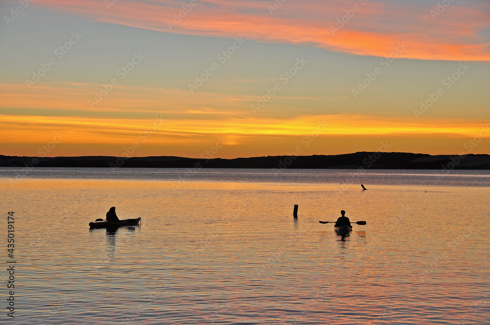 Silhouette of two kayakers watching sunset over lake