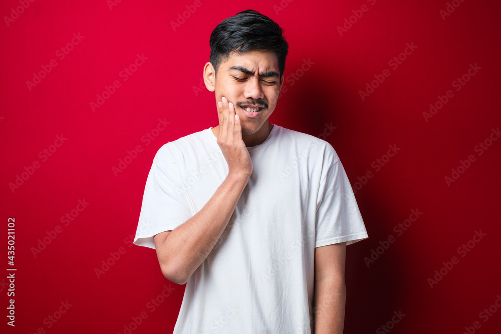 Young handsome man wearing white tshirt standing over touching mouth with hand with painful expression because of toothache or dental illness on teeth. Dentist Young handsome man wearing white tshirt standing over touching mouth with hand with painful expression because of toothache or dental illness on teeth. Dentist