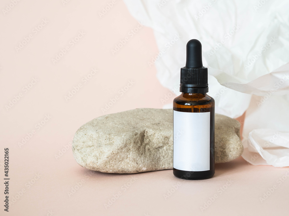 Cosmetic amber glass bottle with white lable next to the stone and white paper