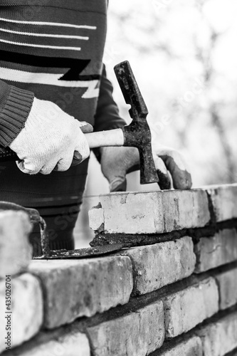 a man builds a wall of bricks, lays a brick on a cement-sand mortar, tapping a brick with a hammer, black and white photo