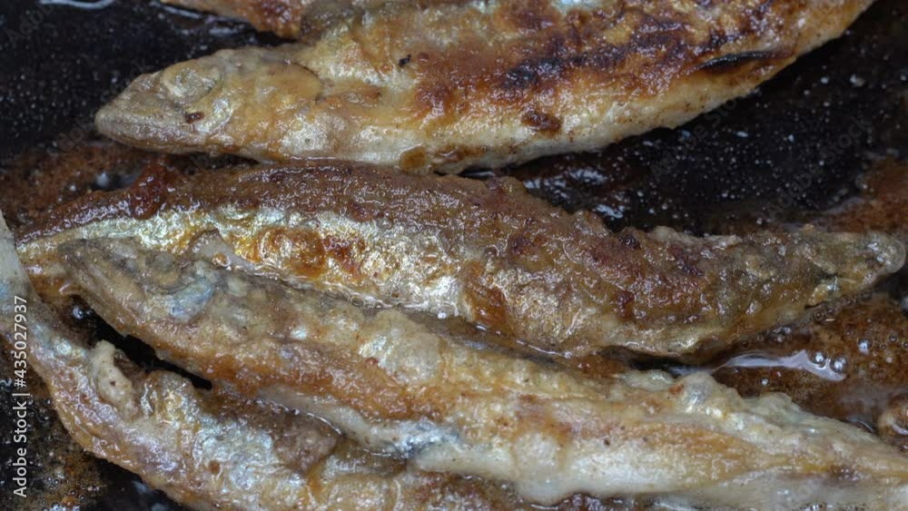 Close-up view cooking frying capelin fish in iron pan. Grilled caplin fish - popular Asian cuisine where entire small fish, from head to tail, roe and bones can be enjoyed as an appetizer or side dish Close-up view cooking frying capelin fish in iron pan. Grilled caplin fish - popular Asian cuisine where entire small fish, from head to tail, roe and bones can be enjoyed as an appetizer or side dish