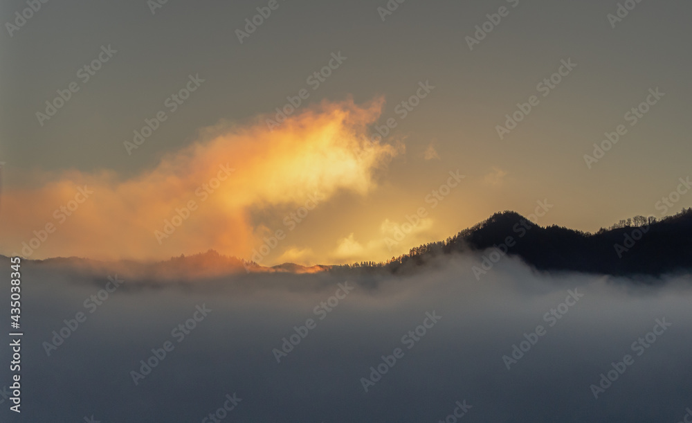 The rising sun forces the mist enveloping the mountain peaks to retreat.