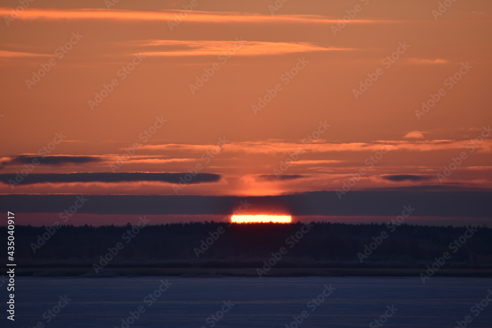 Sunrise over a frozen snow covered lake. Part of sun visible behind clouds Sunrise over a frozen snow covered lake. Part of sun visible behind clouds