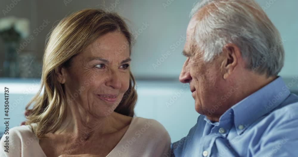 Cinematic shot of lovely happy mature couple enjoying time together is speaking and caressing each other with affection while sitting on sofa at home. Concept: love, family, marriage, happiness, age Cinematic shot of lovely happy mature couple enjoying time together is speaking and caressing each other with affection while sitting on sofa at home. Concept: love, family, marriage, happiness, age