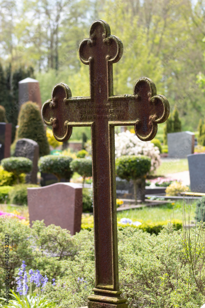 Rusty old cross gravestone on a cemetery, peaceful tomb with other graves and trees in the background Rusty old cross gravestone on a cemetery, peaceful tomb with other graves and trees in the background