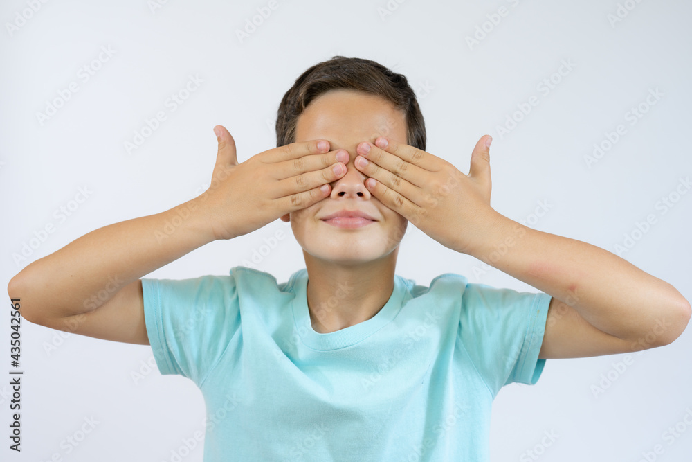Young boy in blue t-shirt covering his face with hands over white background. Young boy in blue t-shirt covering his face with hands over white background.