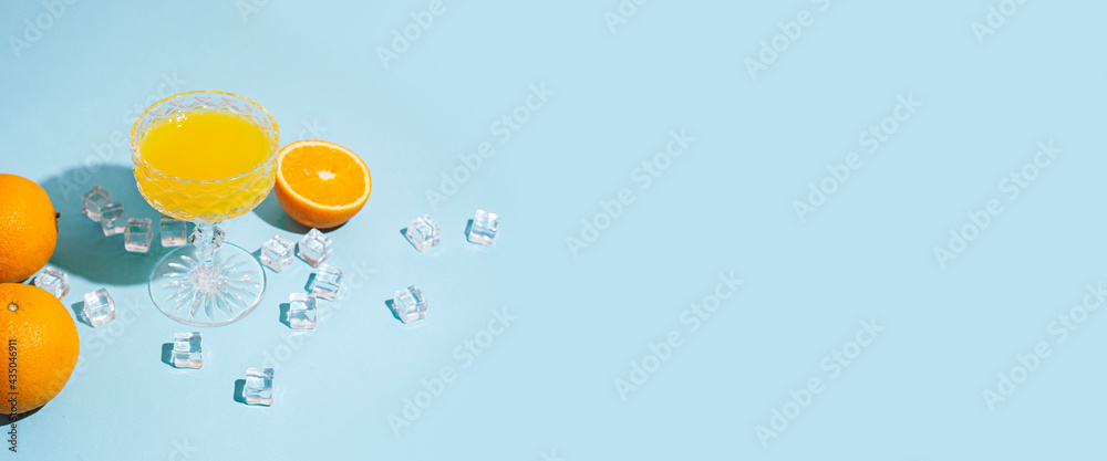 glass with orange juice, orange and ice cubes on a blue background. Banner