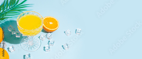 glass with orange cocktail, orange and ice cubes on a blue background. Top view, flat lay. Banner