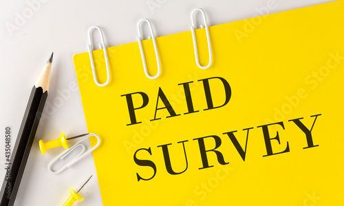 PAID SURVEY word on the yellow paper with office tools on white background