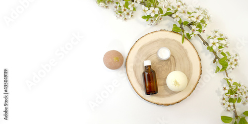 Mock up spa aromatherapy set with essential oil bottle, bath bombs on saw cut and blooming branch. Natural bathe cosmetic products for massage, body and skin care. Eco minimalism. Top view. Banner