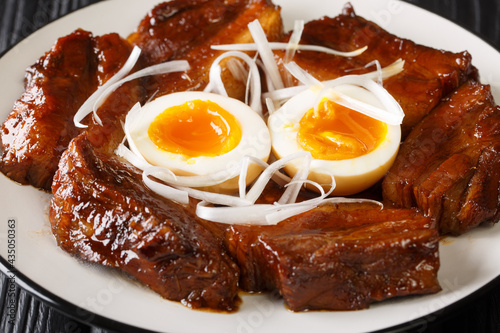 Buta no kakuni is a classic Japanese dish of braised pork belly with boiled eggs close up in the plate on the table. Horizontal