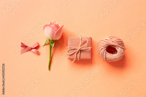 Gift box, ribbon, string, rose flower on orange background. flat lay, top view, copy space