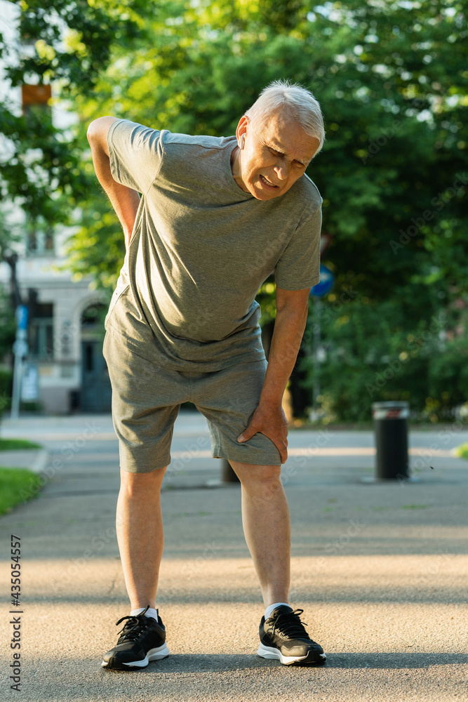 Elderly man suffering from pain in lower back during his jogging workout Elderly man suffering from pain in lower back during his jogging workout