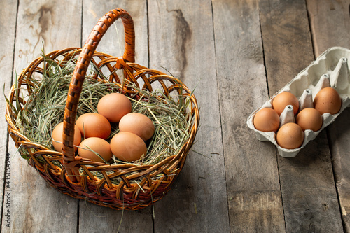 Chicken eggs in a hay basket and egg tray, on a wooden table.