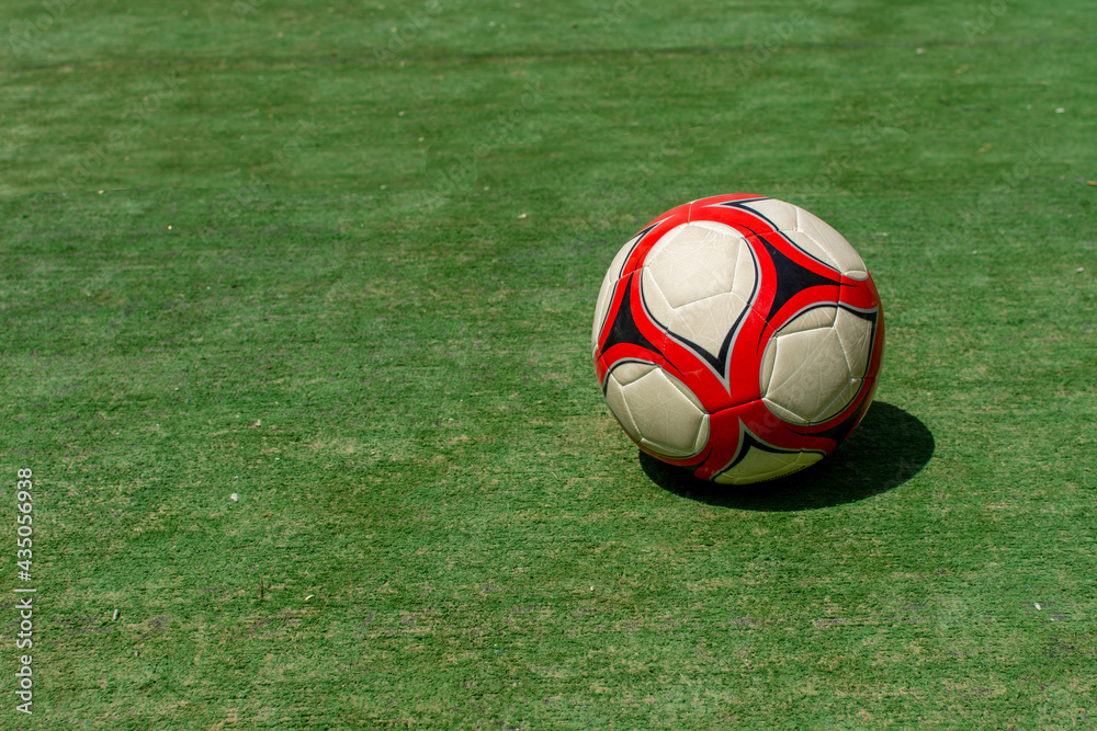 Red and white soccer ball on bright green grass in the sunshine on a summer day for children's recreation. Copy Space. Red and white soccer ball on bright green grass in the sunshine on a summer day for children's recreation. Copy Space.