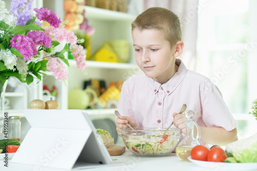 Cute little boy preparing salad on kitchen table at home
