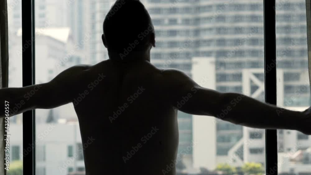 Silhouette of man stretching arms and admire view from window at home, slow motion Silhouette of man stretching arms and admire view from window at home, slow motion