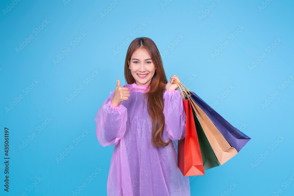 Asian woman holding shopping bags happy excited shopping shopaholic online ecommerce, wearing rain coat raining season concept holiday sales marketing, banner blue isolated background blank copy space