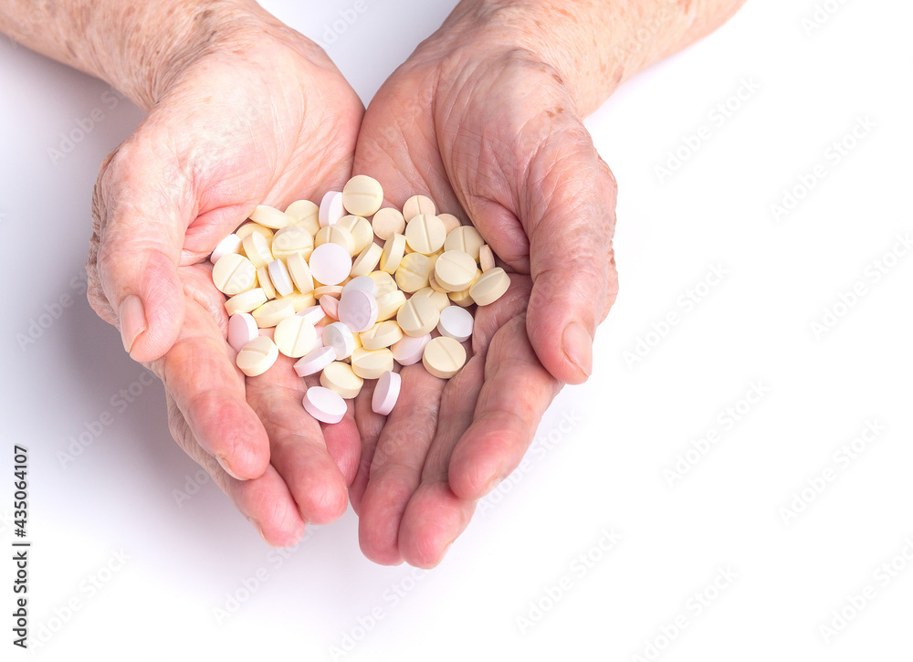 Pills on the palm of a senior woman with a white background. Close-up photo. Aged people and healthcare concept