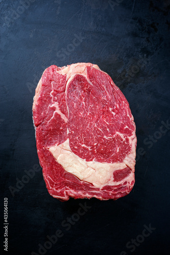 Raw dry aged wagyu rib-eye beef steaks offered as top view on a rustic black board with copy space