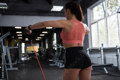 Athletic unrecognizable woman working out with resistance band at gym, rear view shot