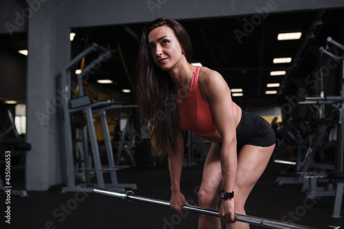 Beautiful athletic sportswoman warming up at the gym, lifting barbell