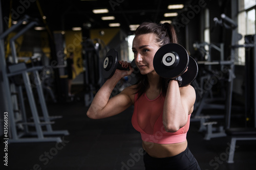Fitness woman working out with dumbbells at functional training gym, copy space
