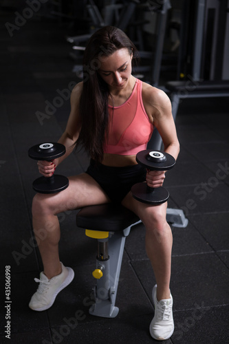 Vertical full length shot of a female bodybuilder exercising with dumbbells