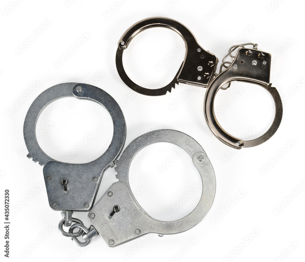 Two pairs of police handcuffs for adults and children isolated on white background with light shadows. Two pairs of real metal handcuffs macro closeup high resolution. Two pairs of police handcuffs for adults and children isolated on white background with light shadows. Two pairs of real metal handcuffs macro closeup high resolution.