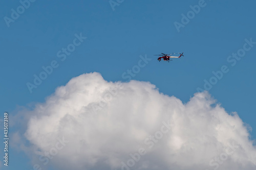 A large red and white fire brigade helicopter flies in the sky above a cloud for a fire rescue