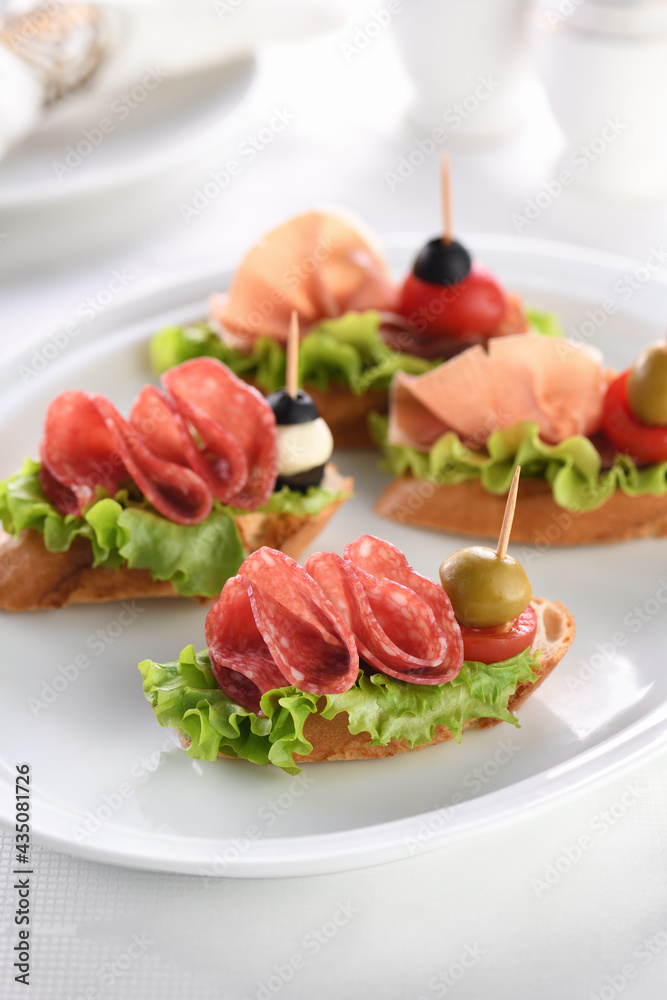 Tender baguette canapes with Leaf lettuce, salami or Parma ham, tomatoes, mozzarella and olive. Delicacy assorted platter for at the party. Tender baguette canapes with Leaf lettuce, salami or Parma ham, tomatoes, mozzarella and olive. Delicacy assorted platter for at the party.