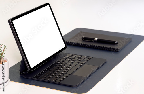 Mockup blank screen tablet with keyboard, notebook and pen on white table.