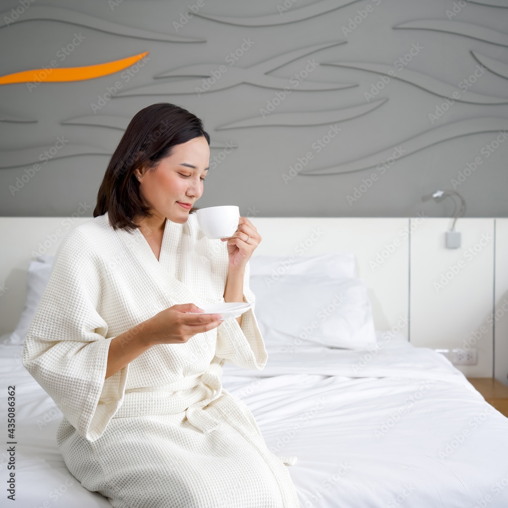 Asian woman in a bathrobe drinking hot coffee on bed in the morning. Asian woman in a bathrobe drinking hot coffee on bed in the morning.