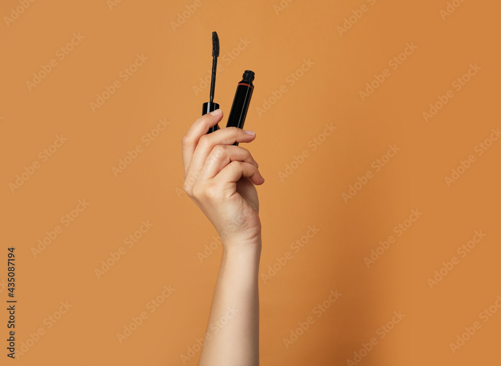 Woman holding mascara on light brown background, closeup. Space for text - obrazy, fototapety, plakaty 