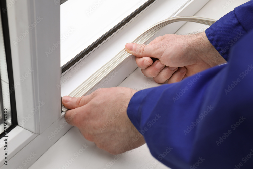 Obraz premium Worker putting rubber draught strip onto window indoors, closeup