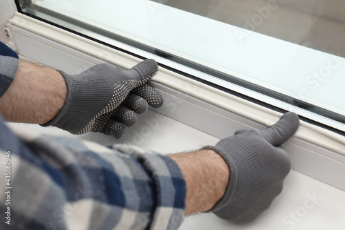 Worker putting rubber draught strip onto window indoors, closeup