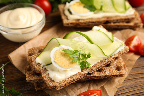 Fresh rye crispbreads with quail egg, cream cheese and cucumber slices on wooden table, closeup