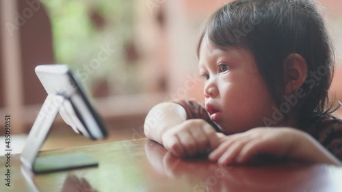 Little cute beautiful girl, Asian people sit and watch their smartphone very focused and intently. The idea of children being too addicted to smartphones in watching cartoons and playing games