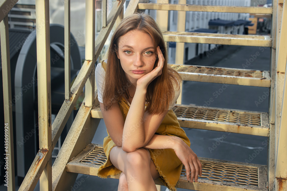 The girl is sitting on an iron ladder. Portrait of a teenage girl. Redhead girl