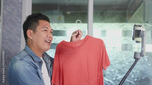 Entrepreneur of Asian young man live streaming video online for selling her dress and clothes to the customer in platform or application online, a hobby concept during a COVID-19 quarantine period.