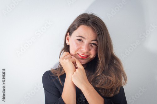Young attractive caucasian girl smiles with hands near face, studio photo isolated on white background.