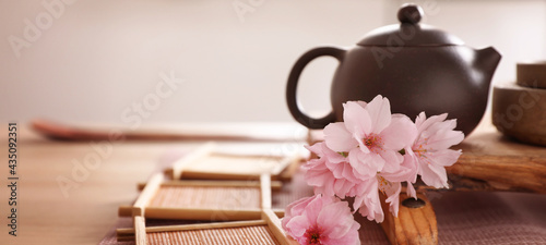 Pot, sakura flowers and bamboo coasters for traditional tea ceremony on table. Banner design photo