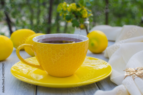 Yellow porcelain cup with tea with a yellow saucer on a wooden table. In the background are yellow lemons.