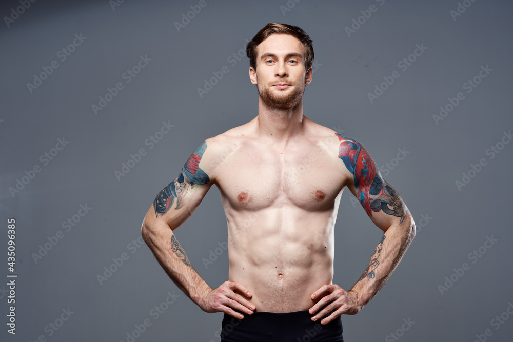 handsome man with a naked pumped-up torso tattoos on his arms holds his hands on his belt handsome man with a naked pumped-up torso tattoos on his arms holds his hands on his belt