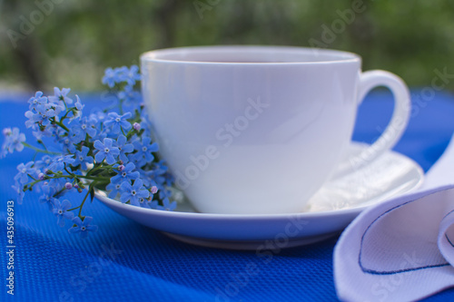 White porcelain cup with tea on the table with blue tablecloth and white napkin.