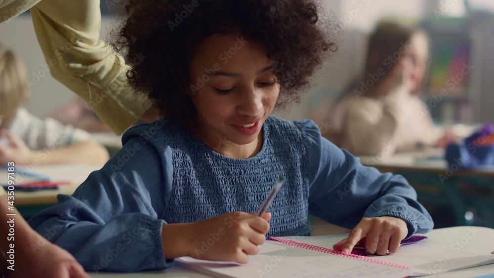 Girl talking with teacher in classroom. Smiling schoolgirl writing in notebook Girl talking with teacher in classroom. Smiling schoolgirl writing in notebook